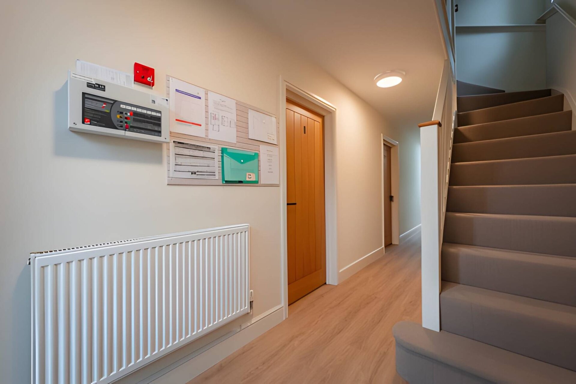 A corridor in a managed building: the fire alarm panel, numbered oak doors and a carpeted stair